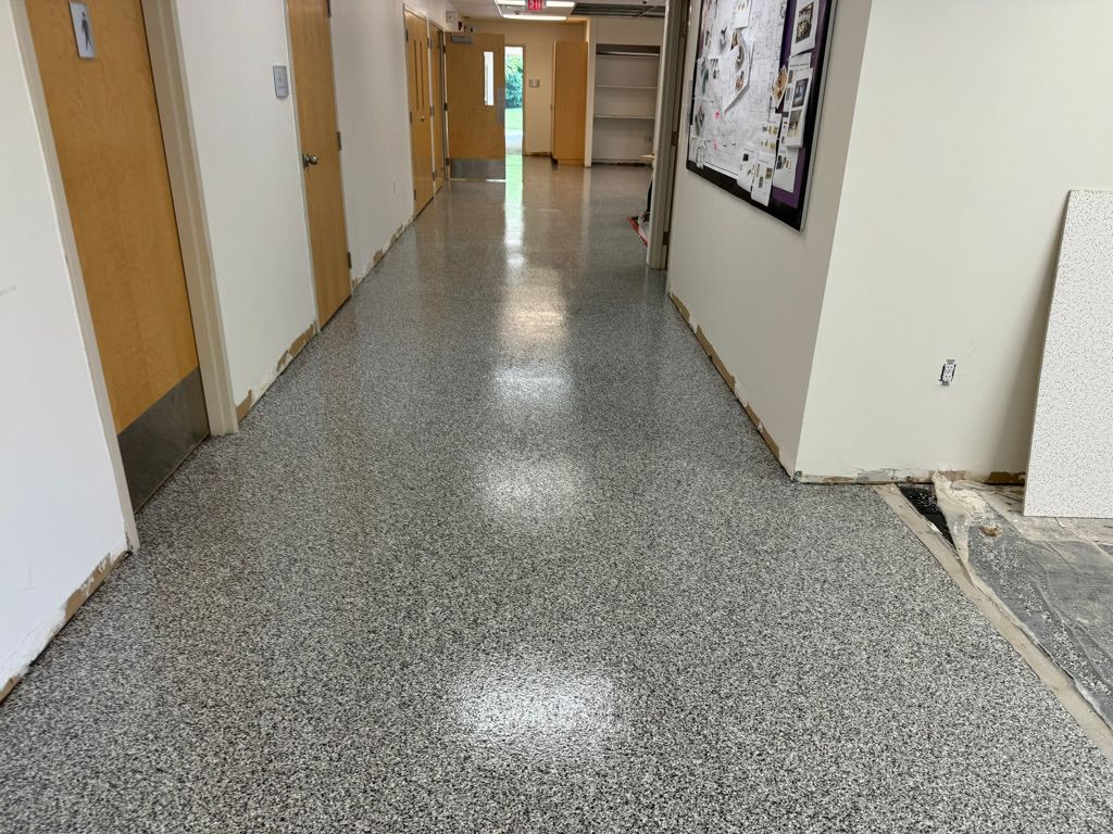 Long school corridor with gray speckled epoxy floor, wooden doors with metal kick plates and bulletin board