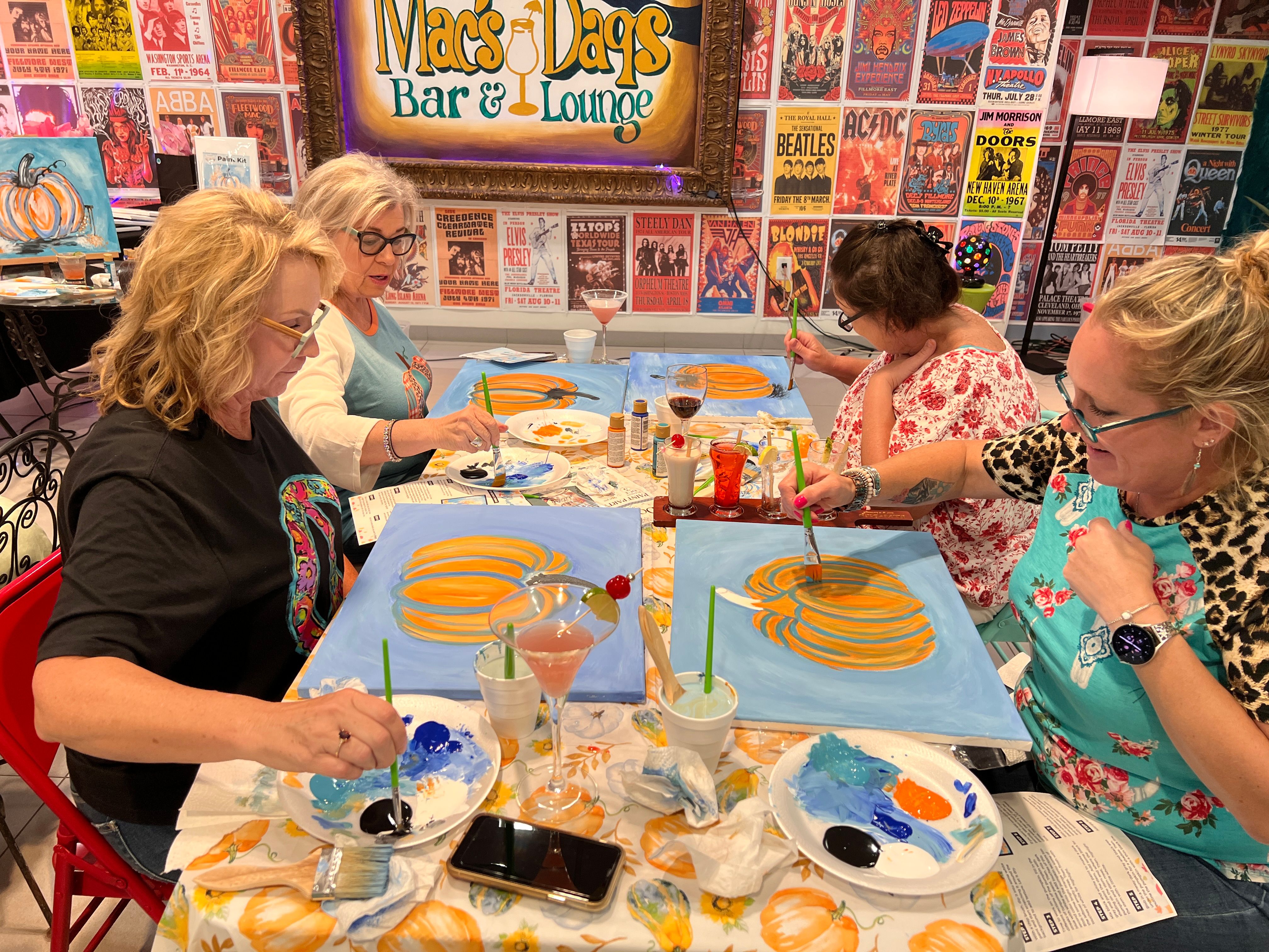 Group painting pumpkins at a fall craft night with drinks