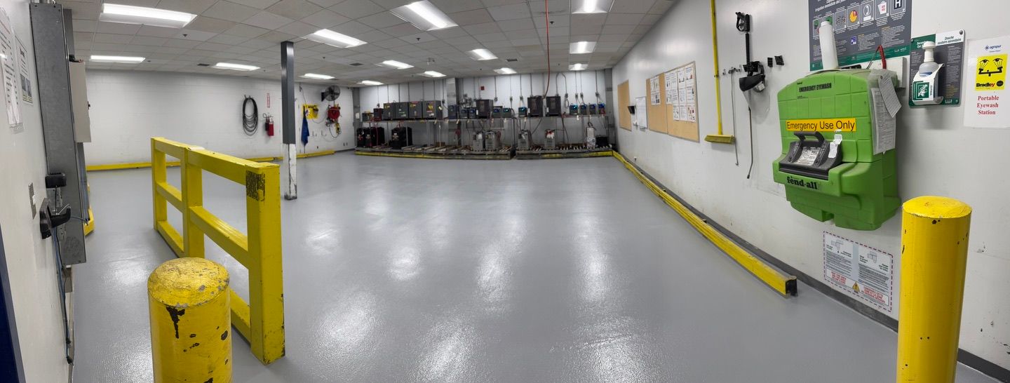 Manufacturing facility with smooth grey epoxy floor, yellow safety railings, emergency eyewash station and control panels