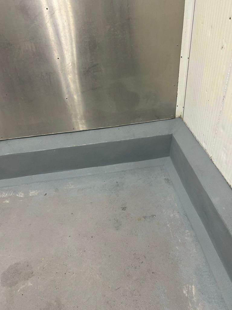 Restored floor-to-wall corner showing smooth gray cove base against metallic panel in commercial food facility