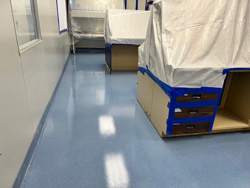 Clean shiny blue epoxy floor installed in a bright pharmaceutical space with furniture and cabinets covered in white protective sheeting