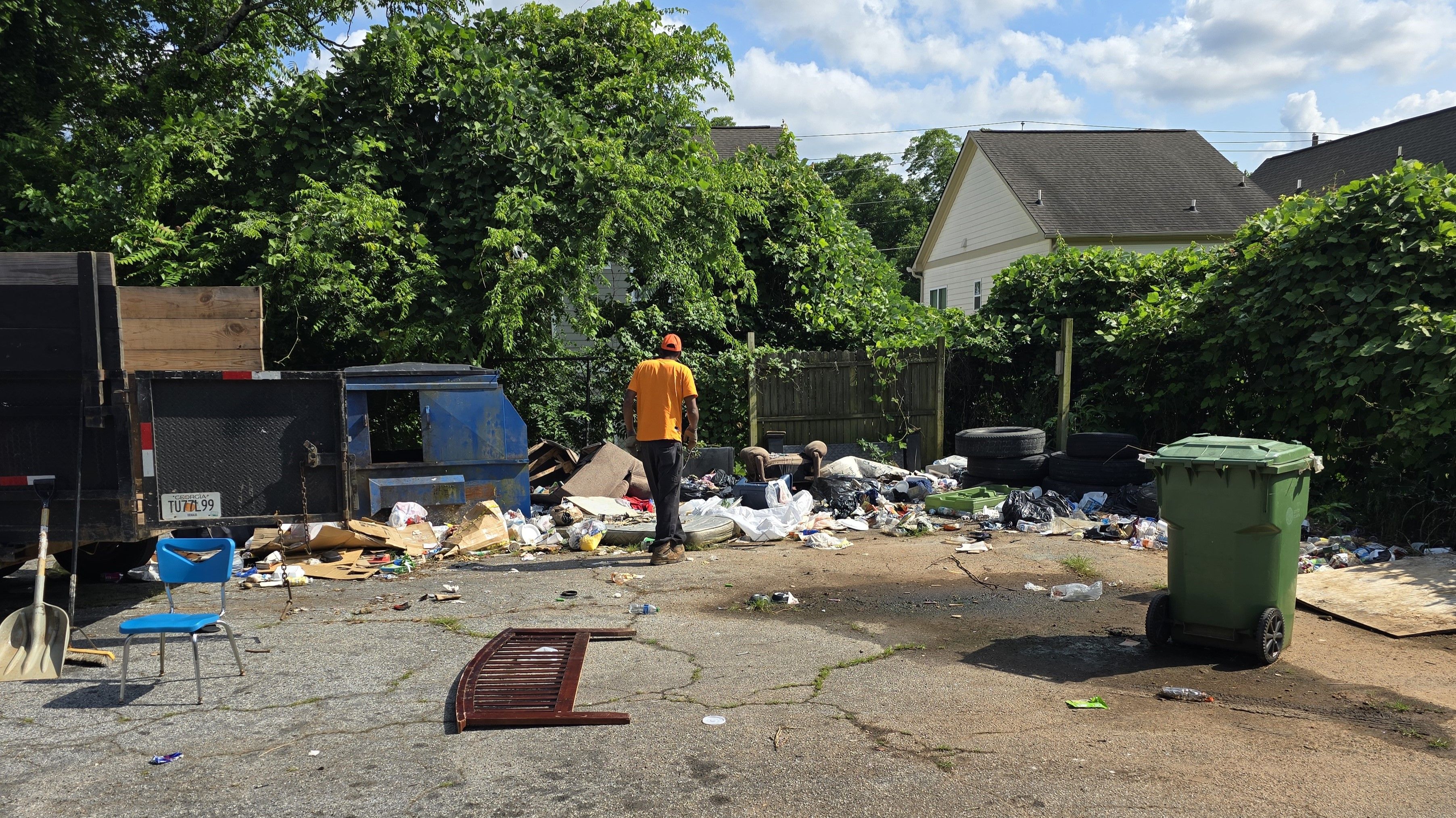 Eviction cleanout job - GoGo Junk Removal technician at job site with black trailer and debris pile