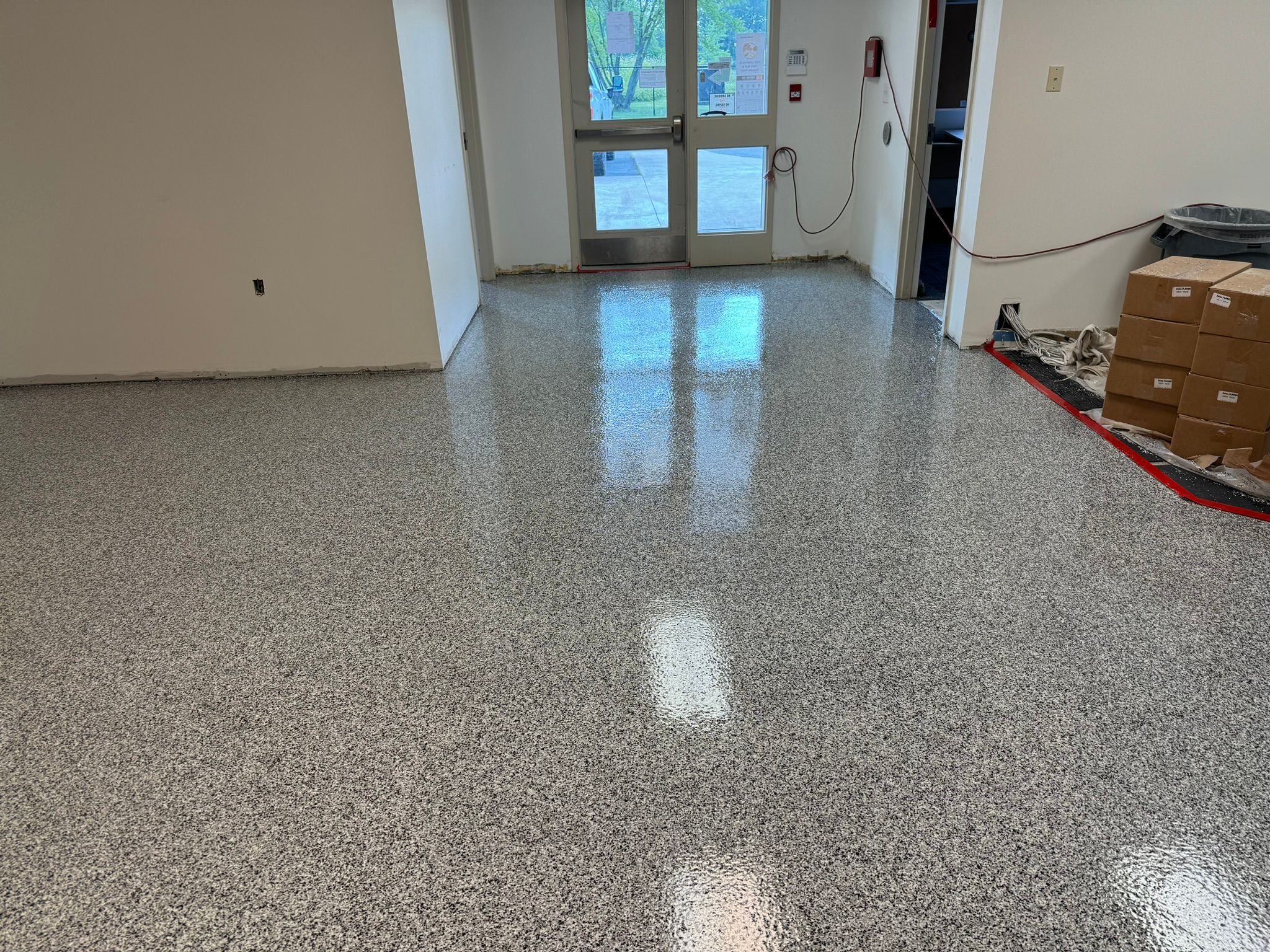 Newly installed speckled gray epoxy floor in school room with glass exterior door, white walls and stacked materials