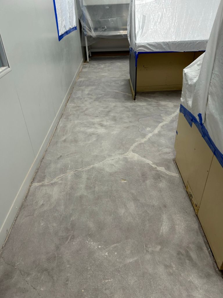 Cracked concrete pharmaceutical floor with furniture and equipment covered in protective sheeting prior to epoxy floor installation