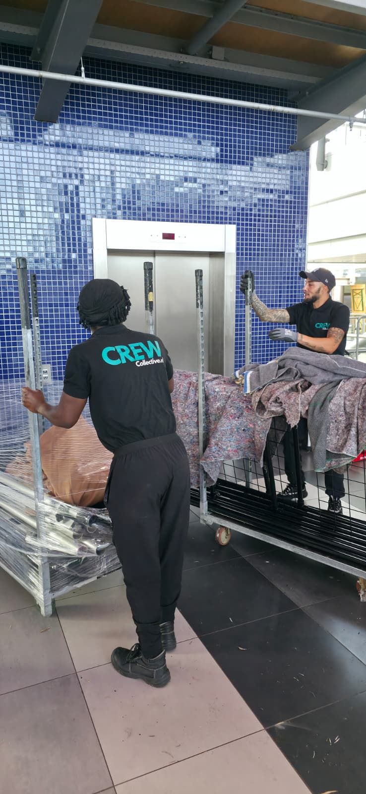 Twee crewleden staan bij een goederenlift en laden materiaal in voor transport naar een hogere verdieping