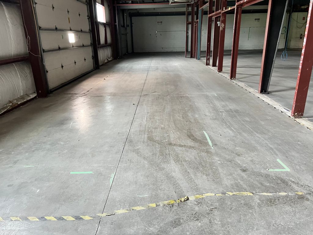 Empty industrial warehouse with concrete floor, red metal beams, large closed garage door and caution tape floor markings