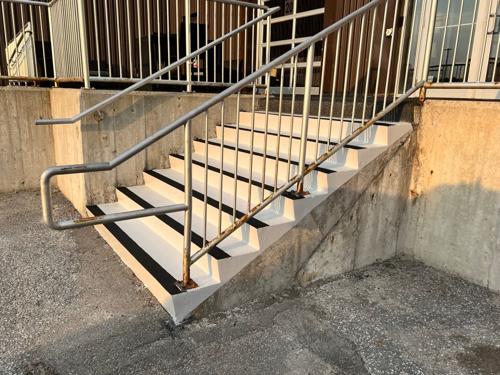 Restored concrete staircase with white epoxy coating and black anti-slip edges at industrial building entrance