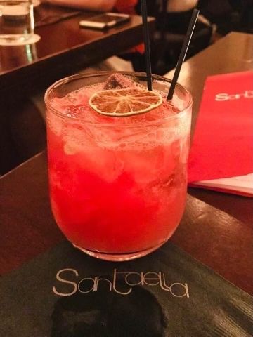 Santaella red cocktail — bright red drink with dried citrus garnish and black straws on a Santaella napkin