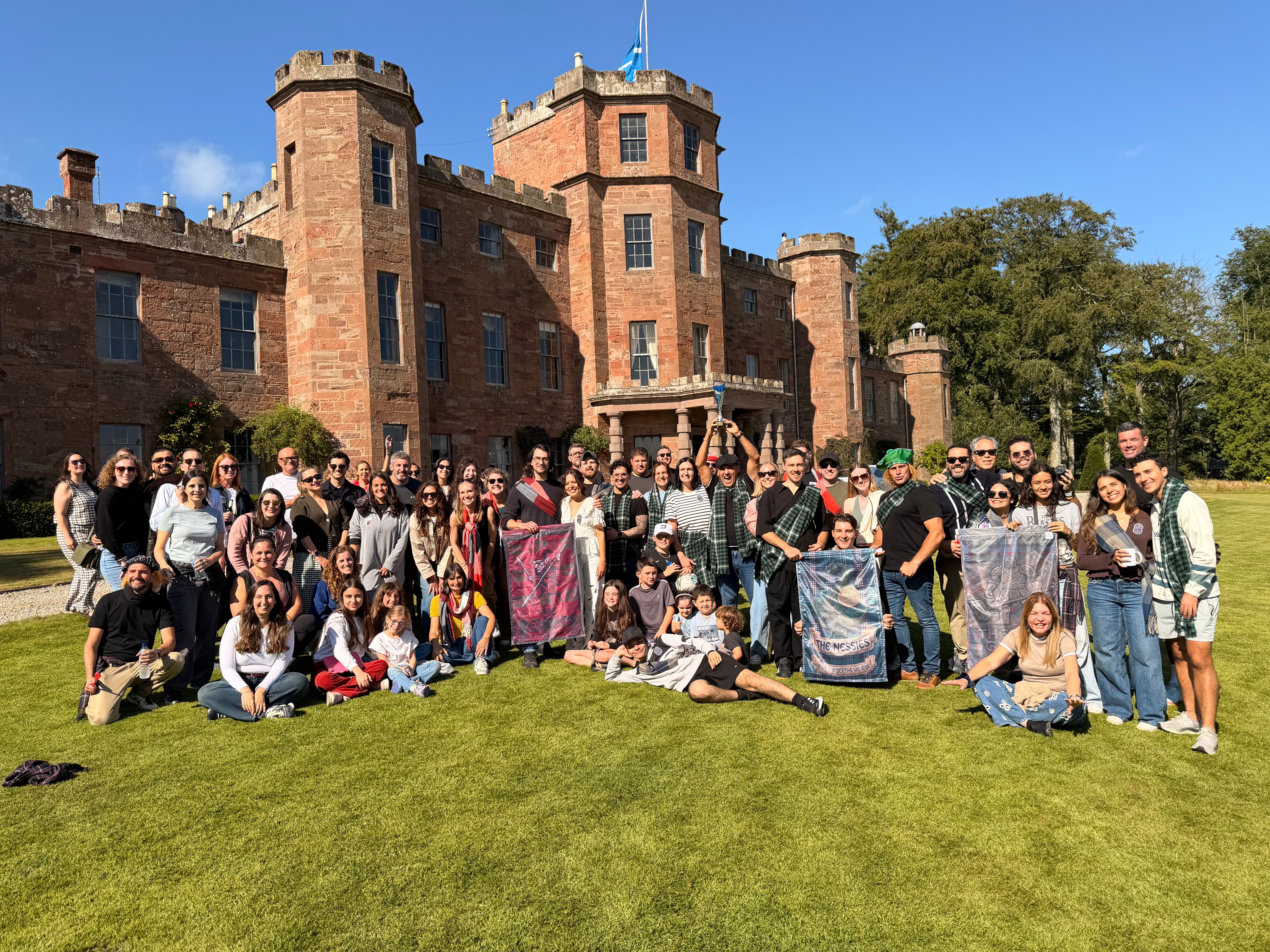 Corporate away day with large group posing in front of a red brick castle — team building and facilitation UK-wide by Event Collection