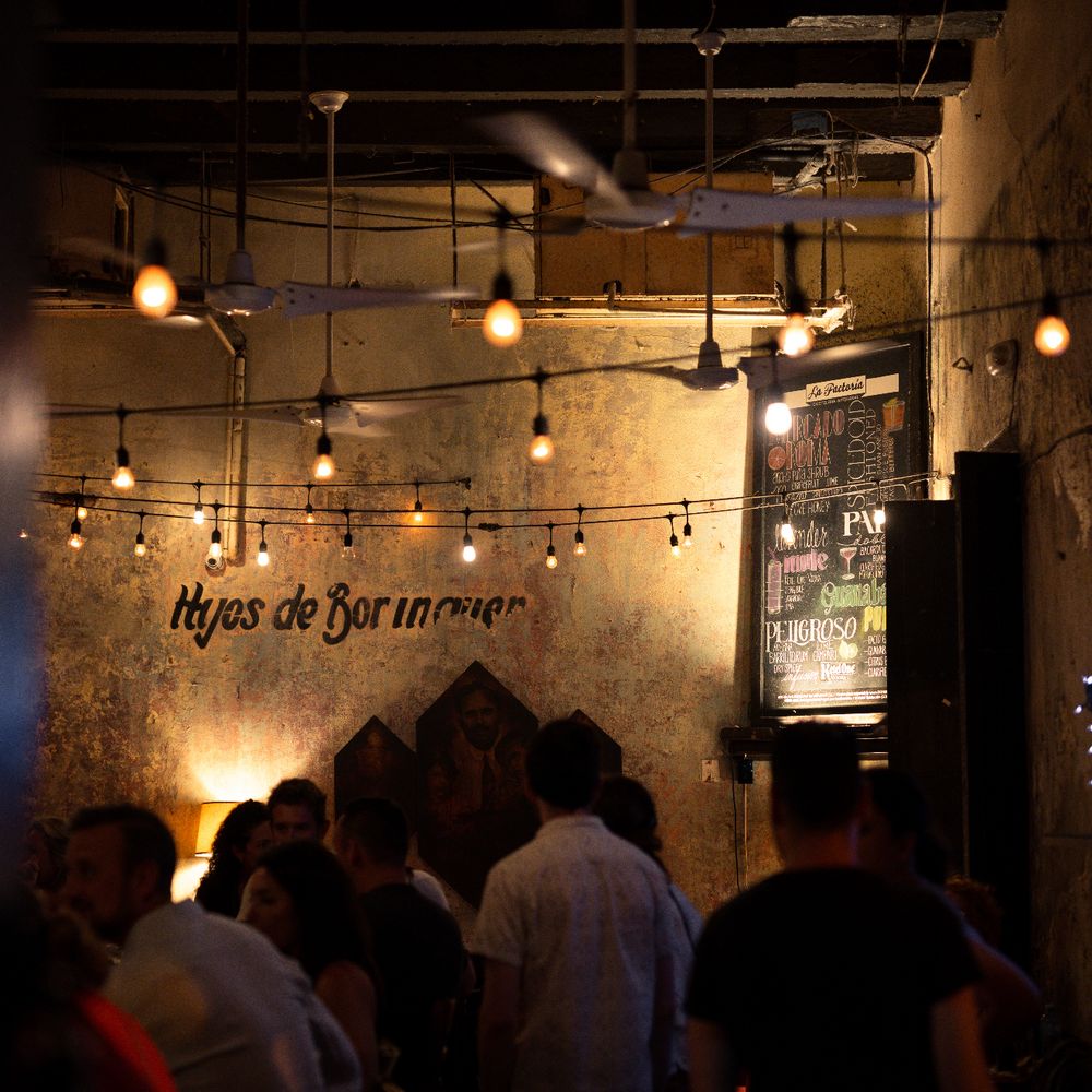 Hijos de Borinquen — guests gathered at La Factoría's front bar with string lights, exposed beams, and warm ambient lighting in Old San Juan