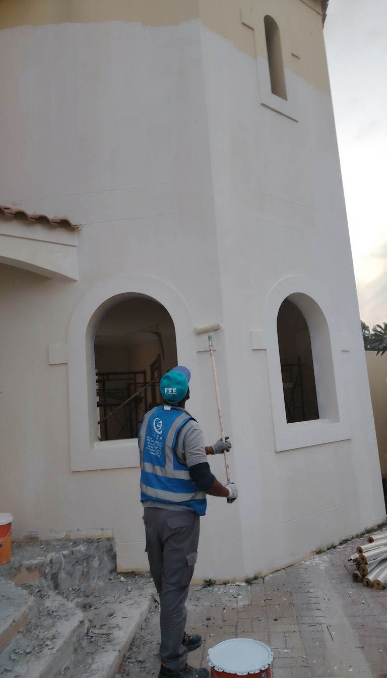 ELCO worker in branded blue vest painting exterior wall of building