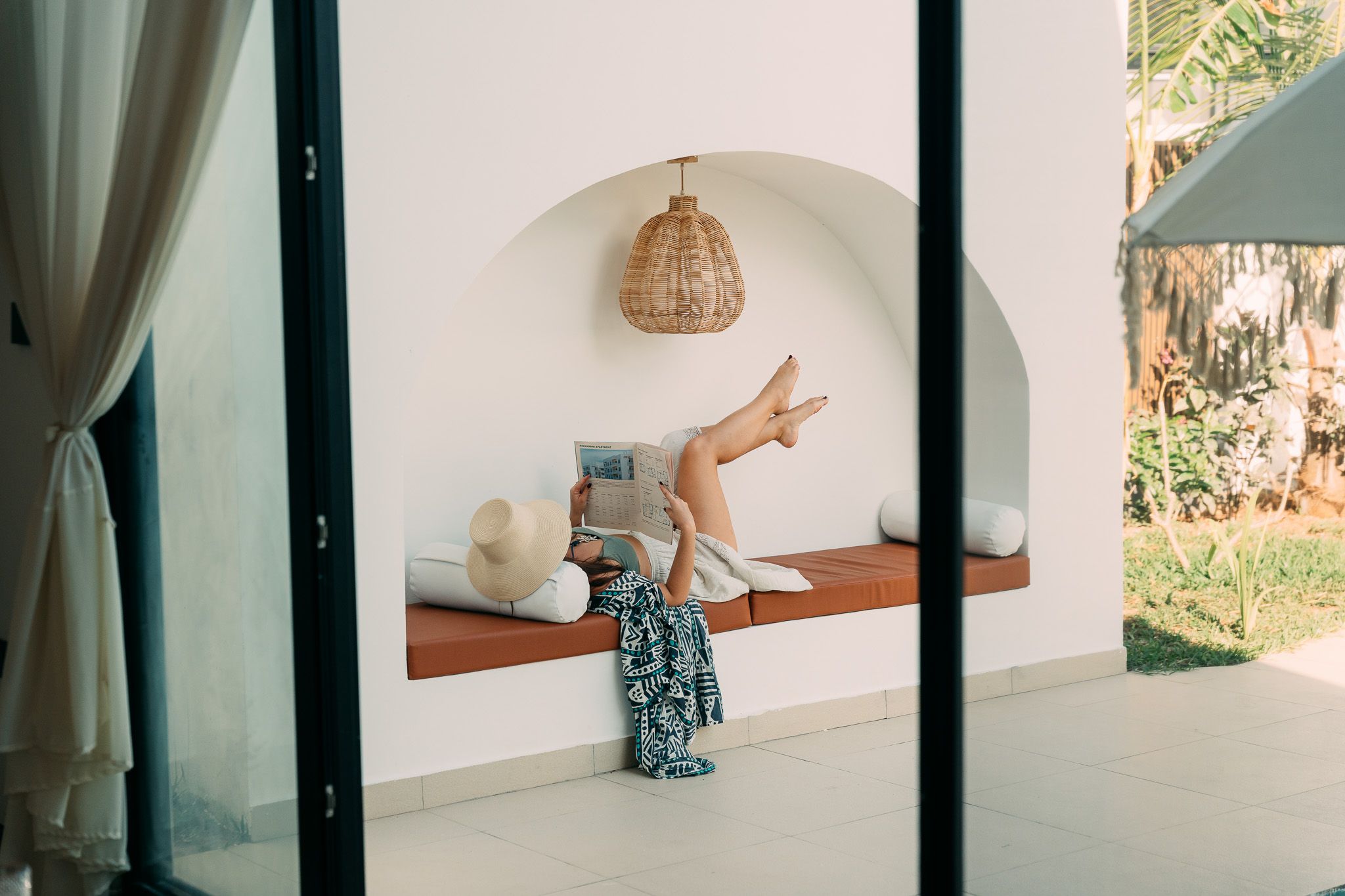 Guest relaxing on outdoor bench with hat and magazine — Airbnb lifestyle photography Zanzibar