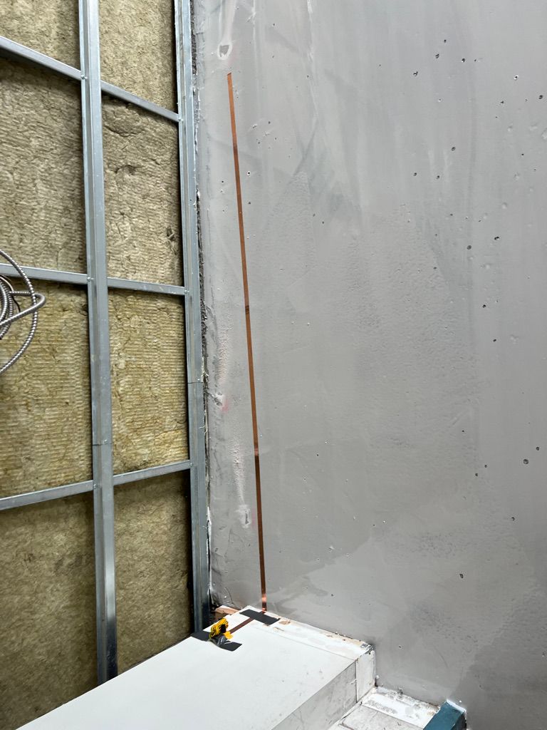 Room corner with gray wall and metal framing, vertical copper ESD grounding strip and small yellow marker at base