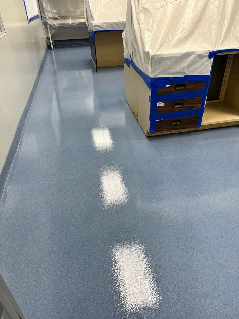 Shiny light blue pharmaceutical epoxy floor reflecting overhead lighting in a narrow lab corridor with protected cabinetry along the wall