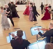 Couples dancing with violinists playing in the foreground, formal ballroom with mirror backdrop