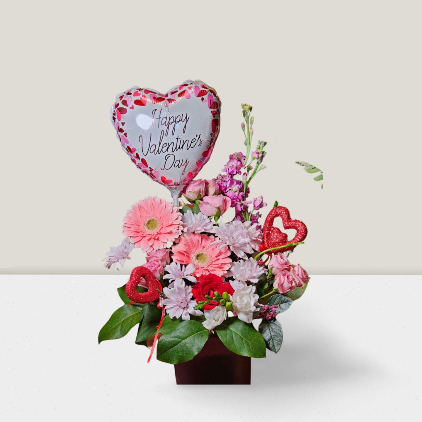 Valentine's Day arrangement with pink gerberas, hearts, and festive balloon
