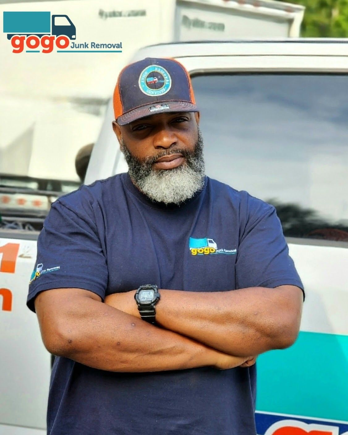 GoGo Junk Removal owner Tyron Holmes in branded navy shirt and cap standing by company truck in Decatur GA ready for same-day junk pickup