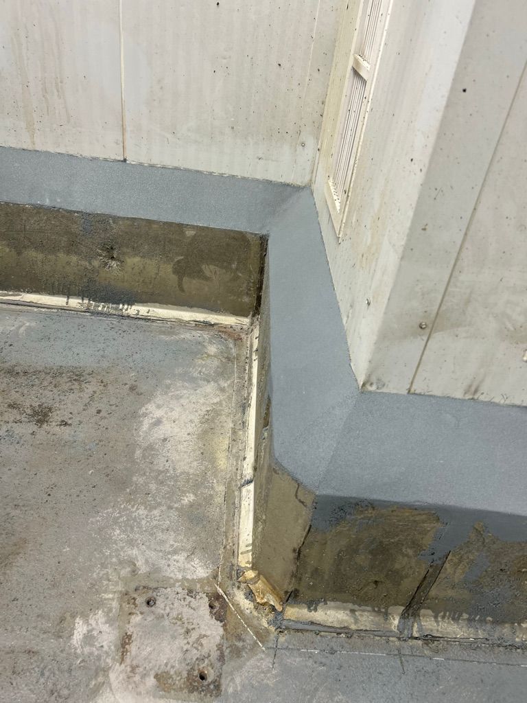 Restored wall and floor junction showing smooth gray polymer cove base with vent on white panel wall