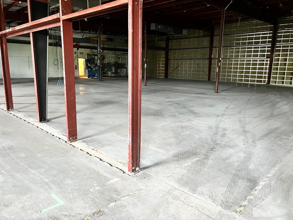 Empty industrial warehouse with concrete floor, red metal beams with black panels and blue scissor lift near bright open doorway