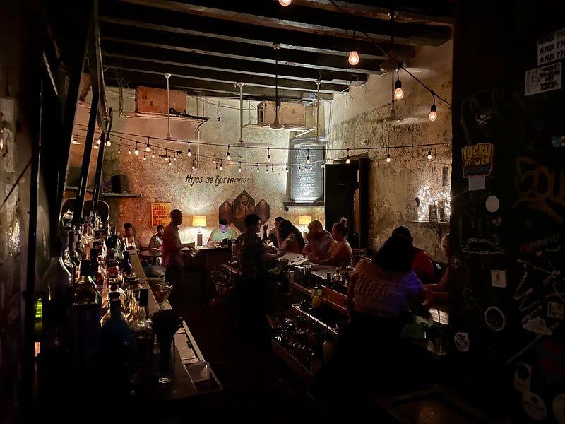 Hijos de Borinquen — guests gathered at La Factoría's front bar with string lights, exposed beams, and warm ambient lighting in Old San Juan