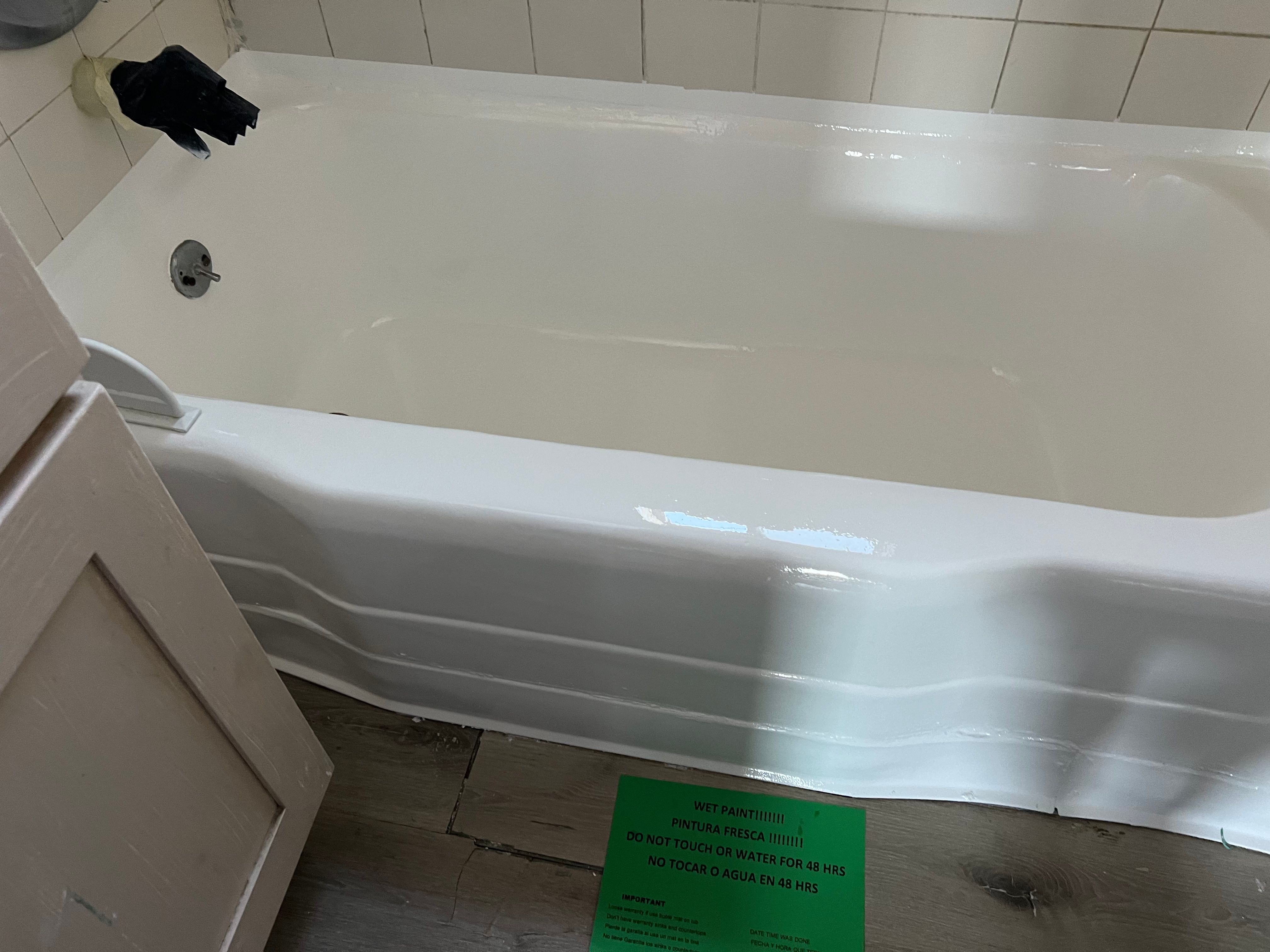 Bathtub after reglazing — bright white finish with wet paint sign by PMR Projects