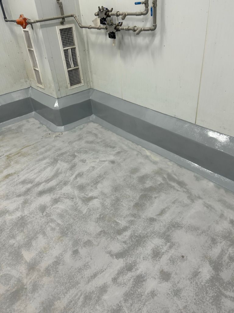 Completed room with smooth gray speckled floor, seamless cove base, vents and pipe assembly with valves after restoration