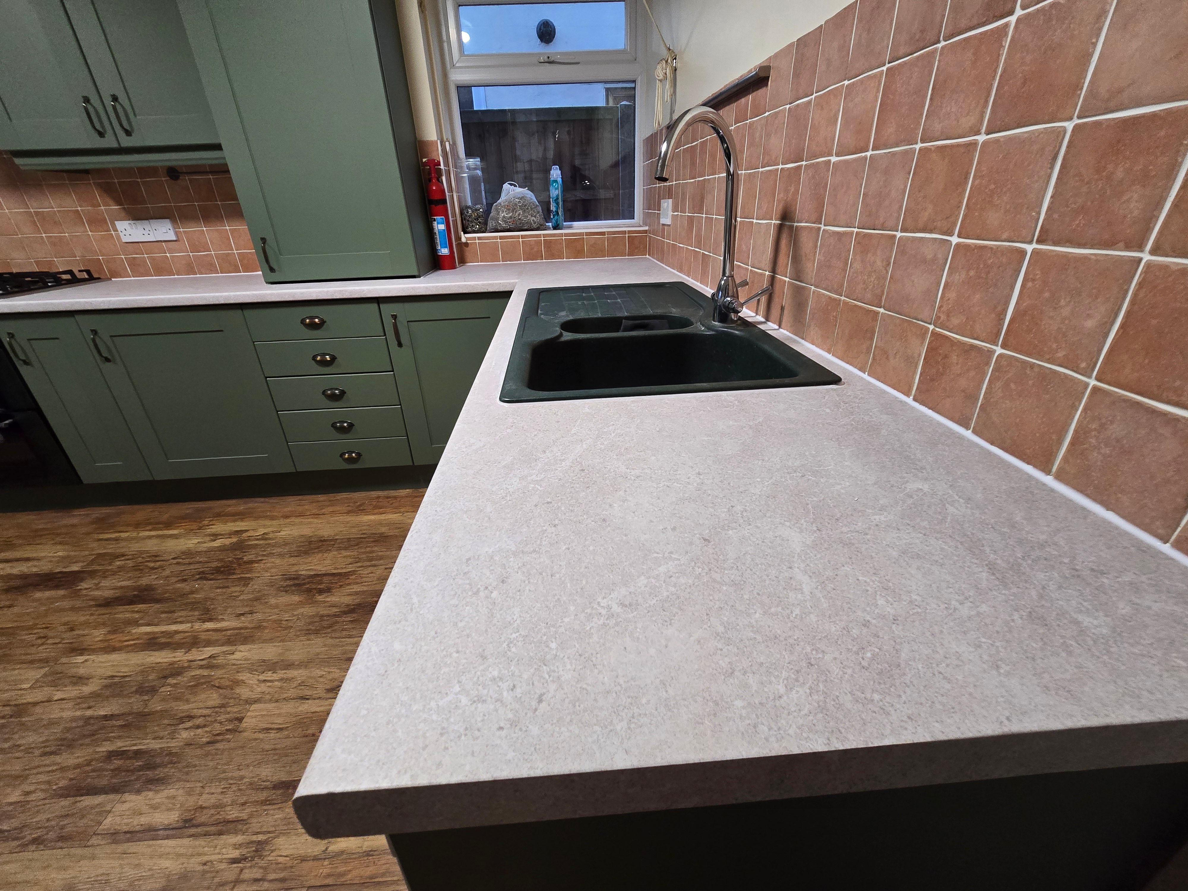 Kitchen after wrapping — close-up of sage green wrapped doors with stone-effect worktop and black sink