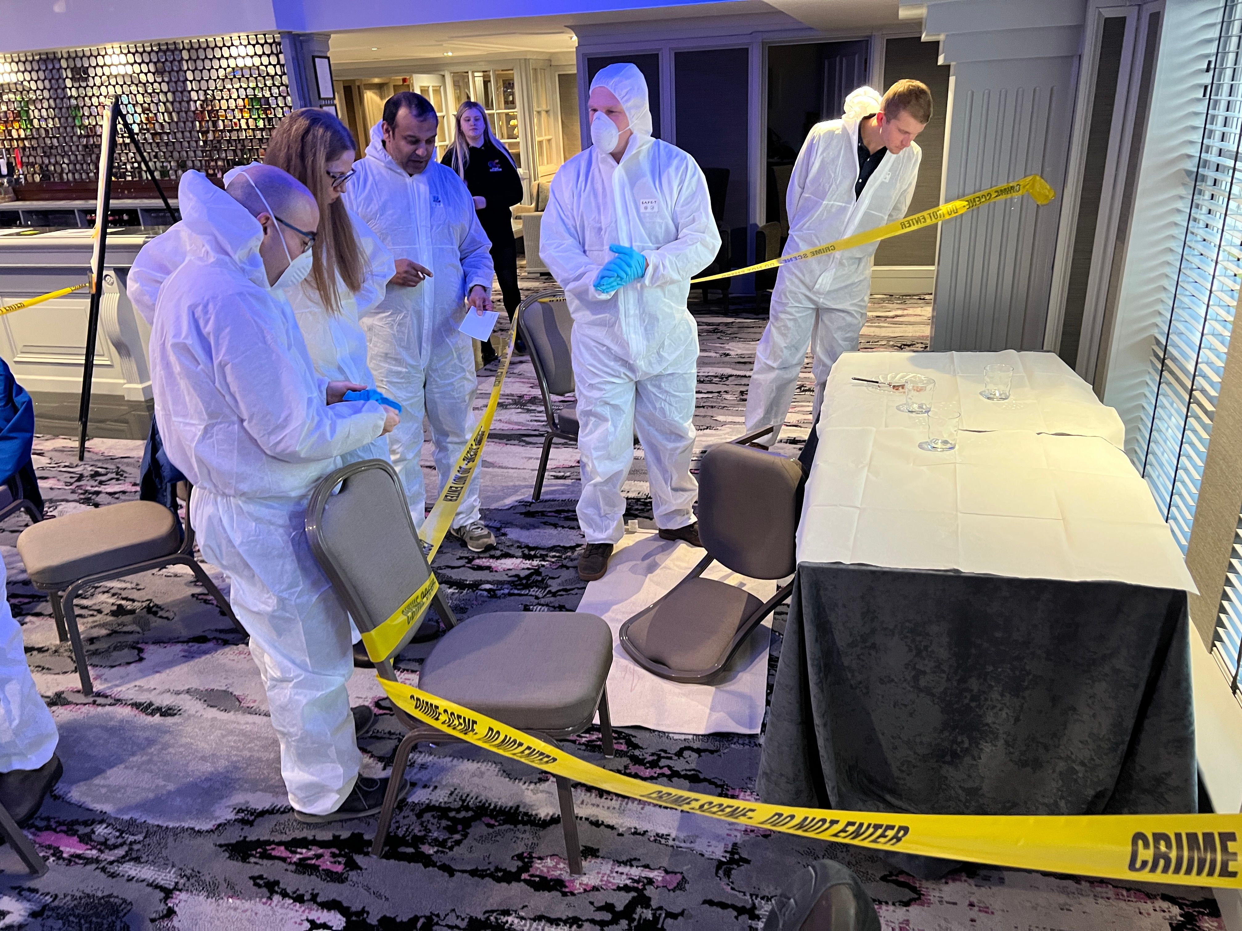 Teams in forensic suits examining crime scene evidence with yellow caution tape