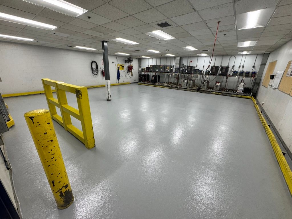 Empty industrial maintenance room with smooth light grey epoxy floor and yellow safety barrier