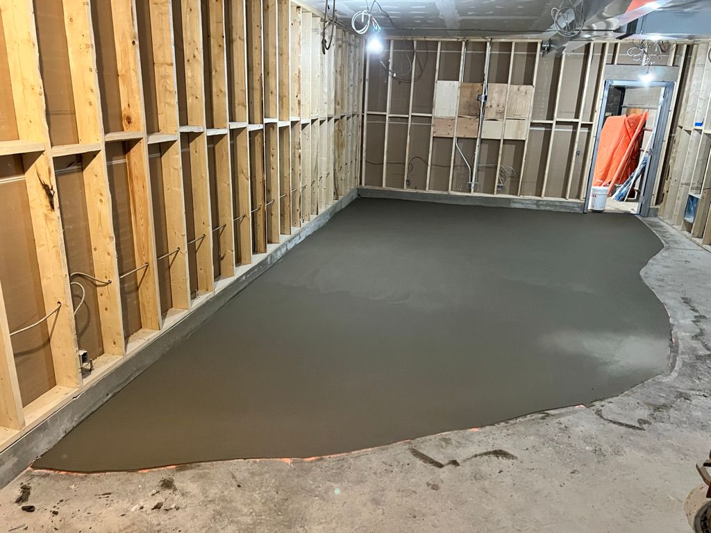 New concrete slab partially poured in unfinished commercial room with wood-framed walls and exposed wiring