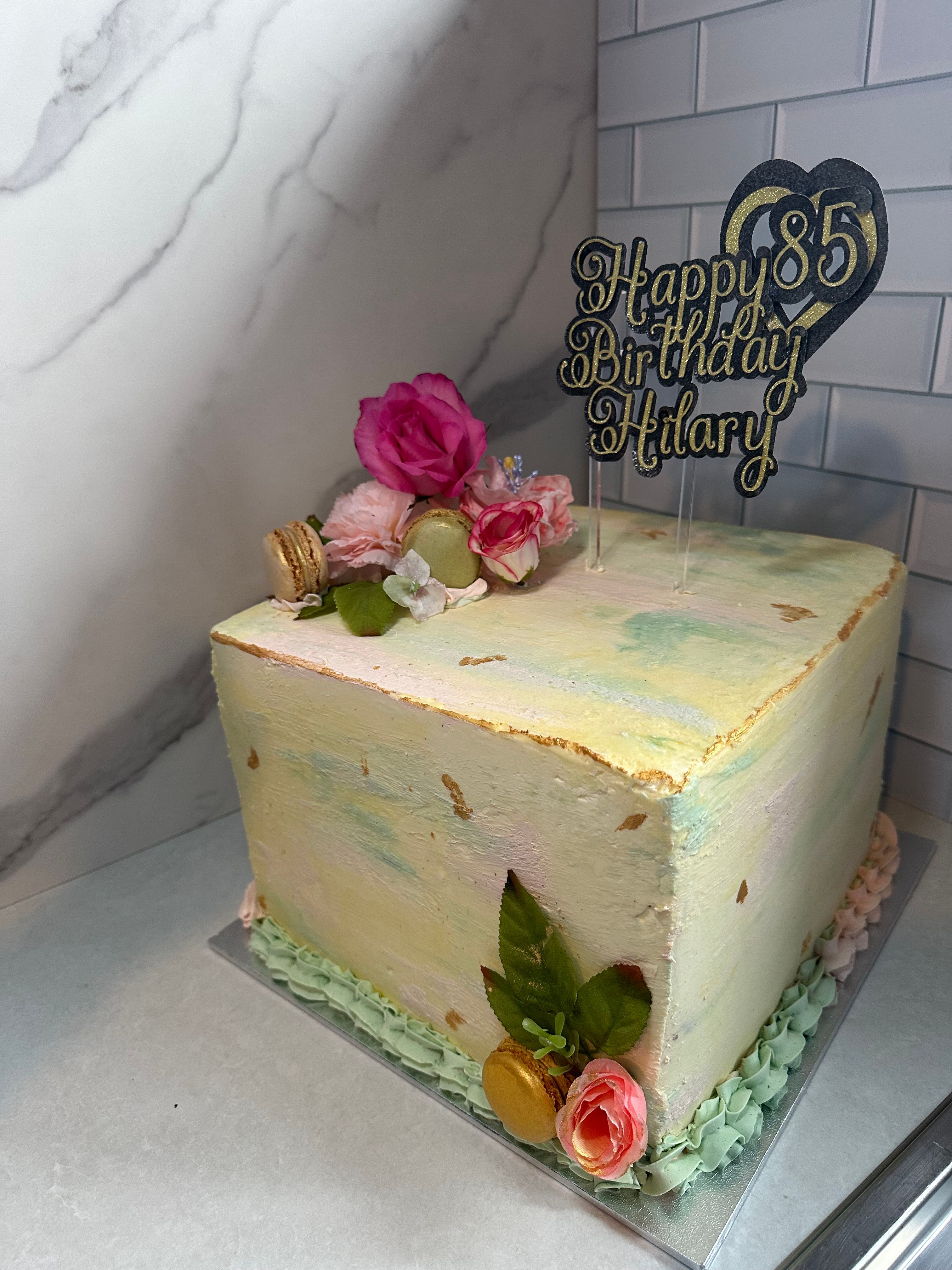 Side view of square watercolour buttercream cake with florals and topper