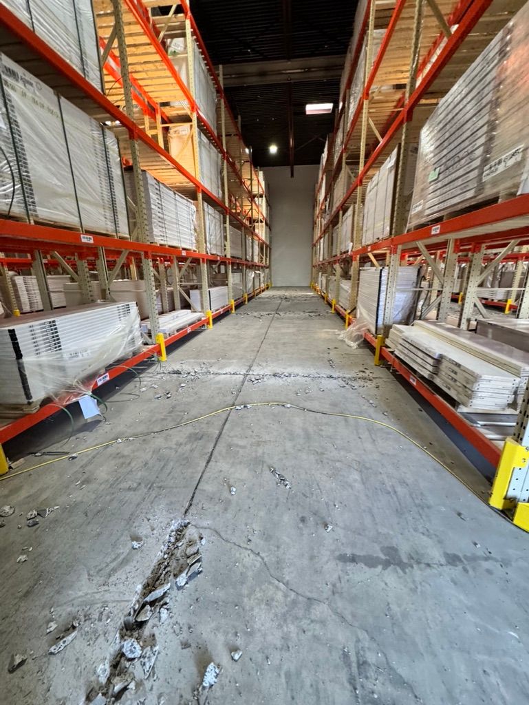Warehouse aisle before-shot with cracked concrete floor trench and orange shelves stocked with wrapped product