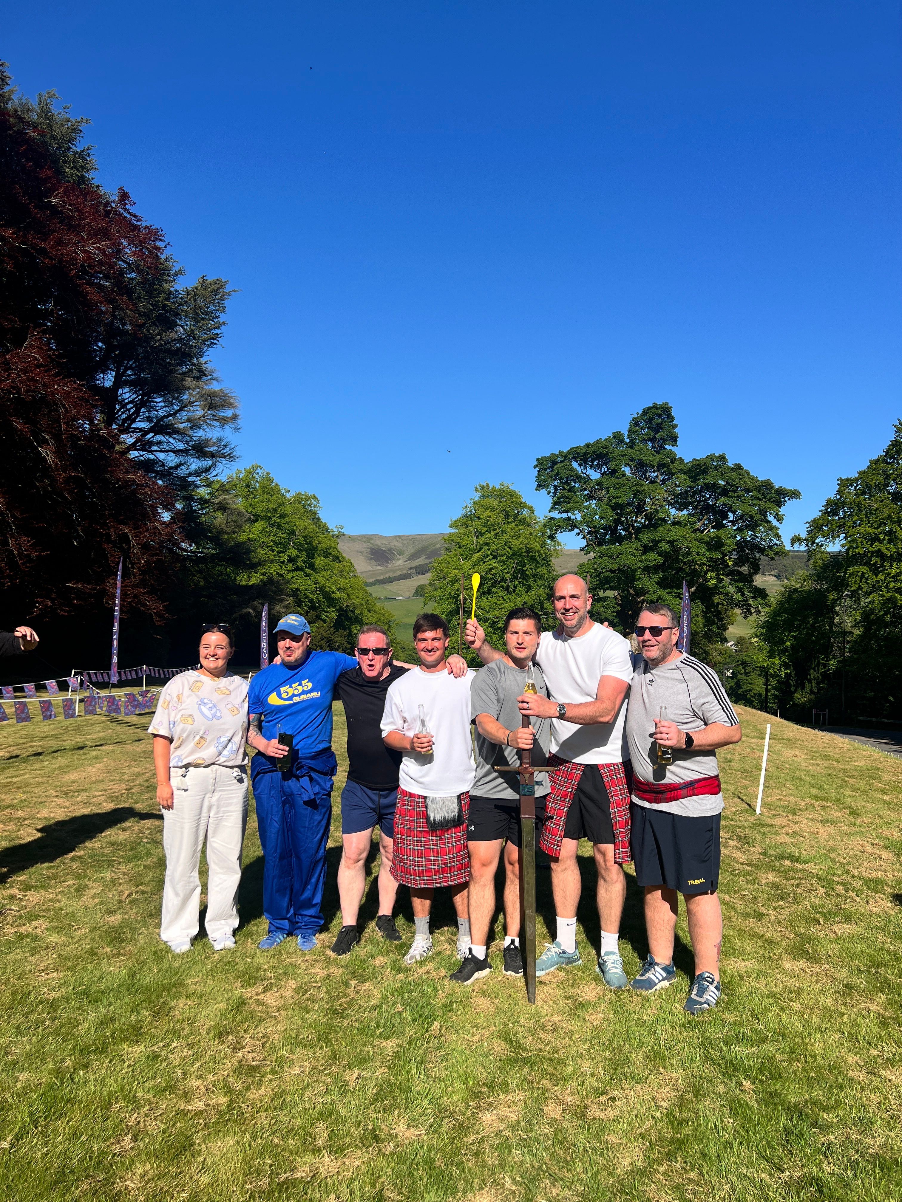 Highland Games corporate team building event — seven participants in kilts competing outdoors with sword and spoon challenges