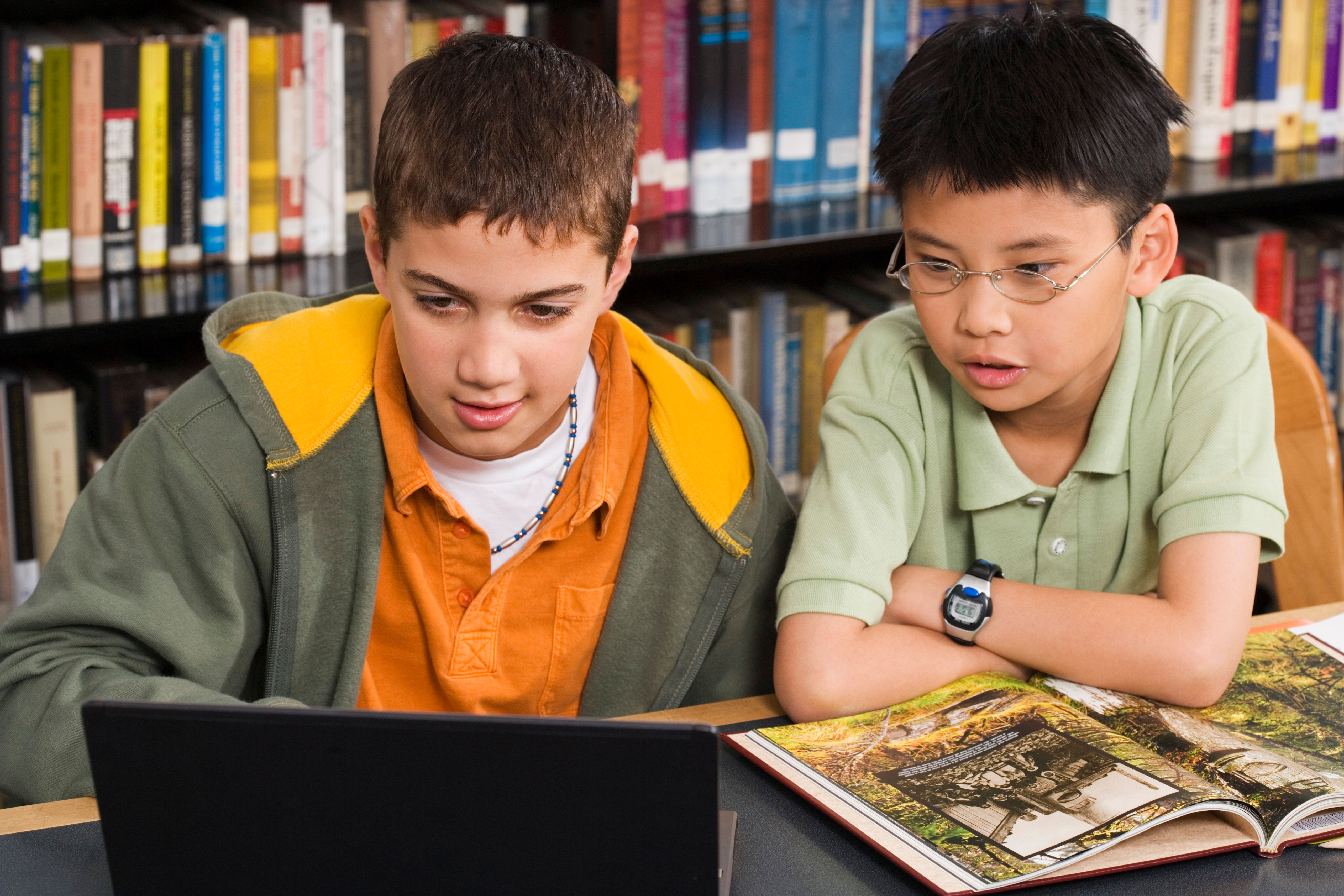 Two boys studying together with a laptop and books in a library