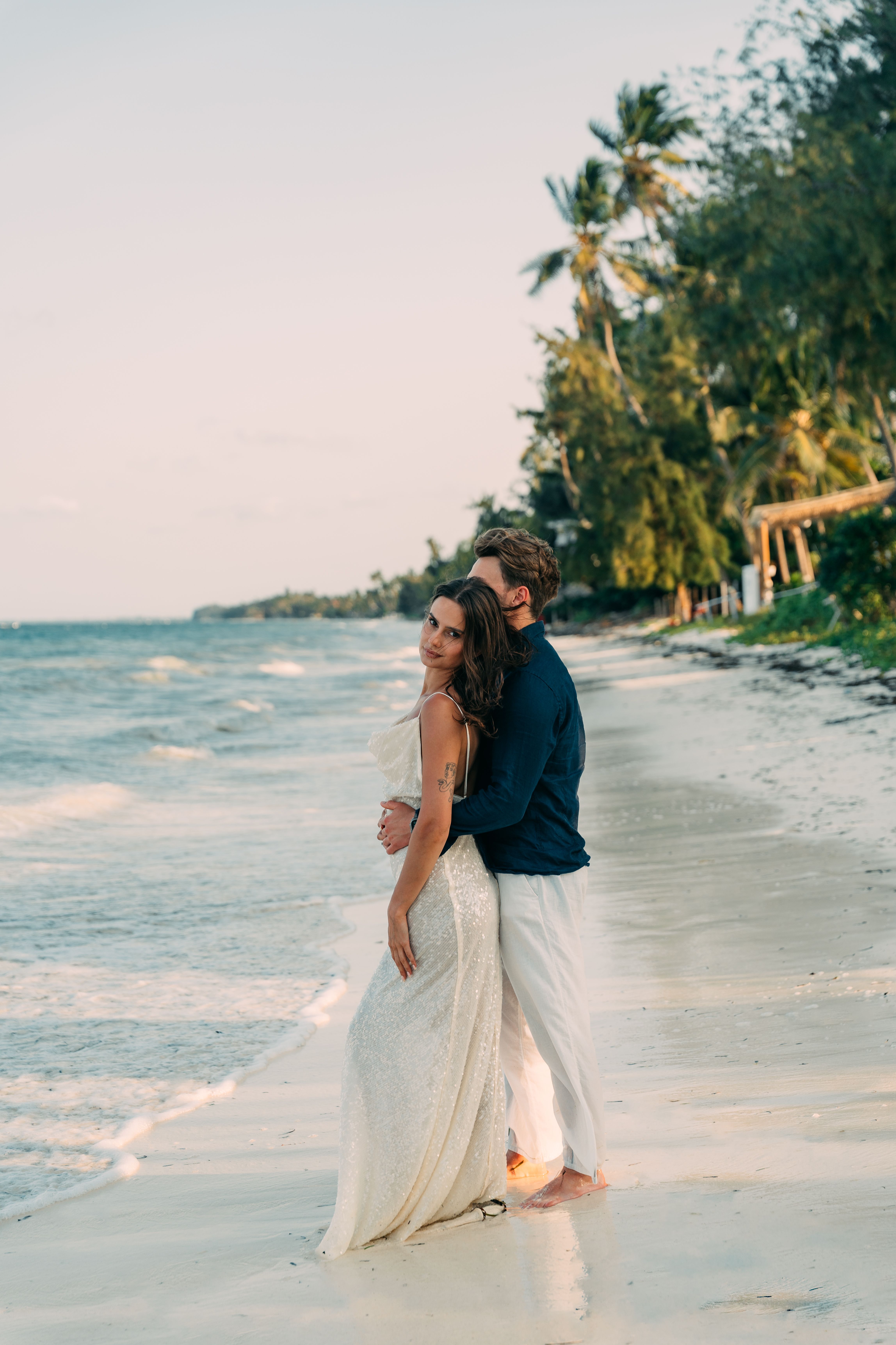 Romantic couple on Zanzibar beach - woman in white dress with palm trees