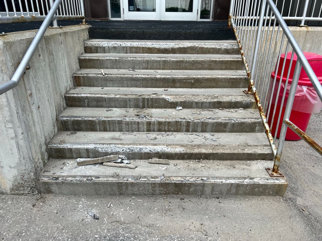 Six-step concrete staircase showing visible damage and debris before repair — metal railings with rust and red waste bin