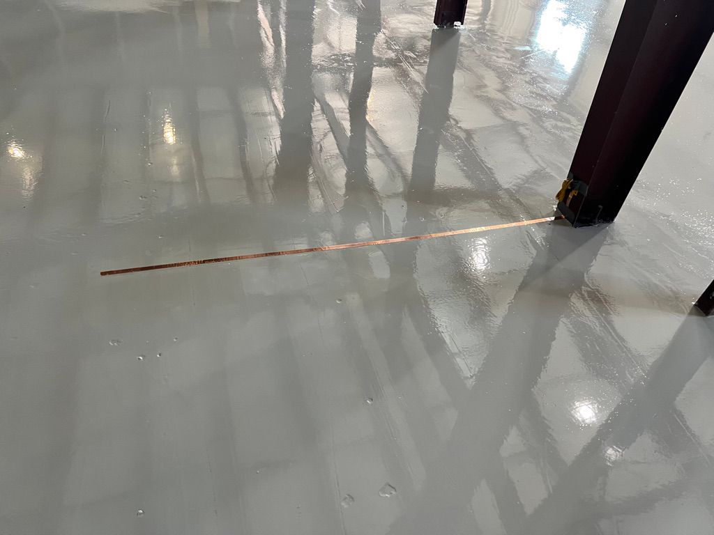 Smooth shiny gray ESD floor with copper grounding strip running horizontally between vertical metal beams