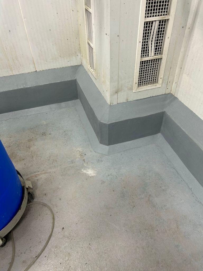 Completed room with gray seamless floor, dark gray cove base strip, vents and blue barrel — after cove base restoration