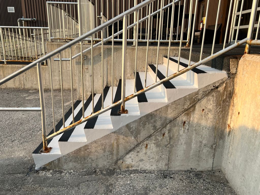 Concrete staircase after restoration with white epoxy steps and black anti-slip strips — metal railings in sunlight