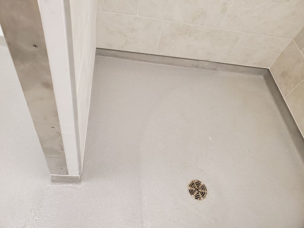 Healthcare facility clean room corner with tiled walls, smooth light gray seamless floor and circular metal floor drain