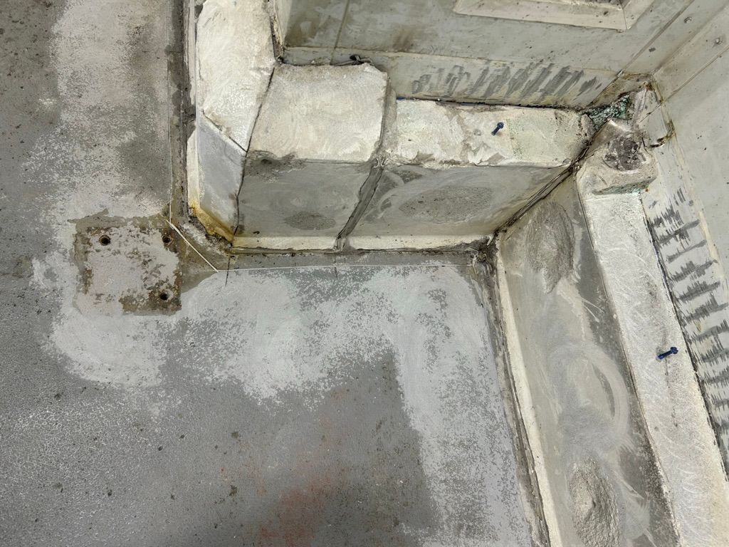 Close-up of damaged concrete corner showing cracks, chips and anchoring screws before restoration