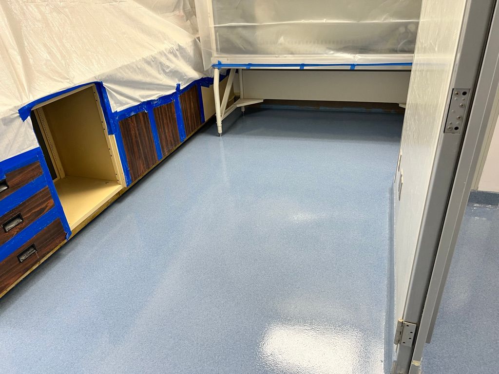 Light blue seamless epoxy floor installed in a pharmaceutical lab, wooden cabinets and equipment protected with plastic sheeting during installation
