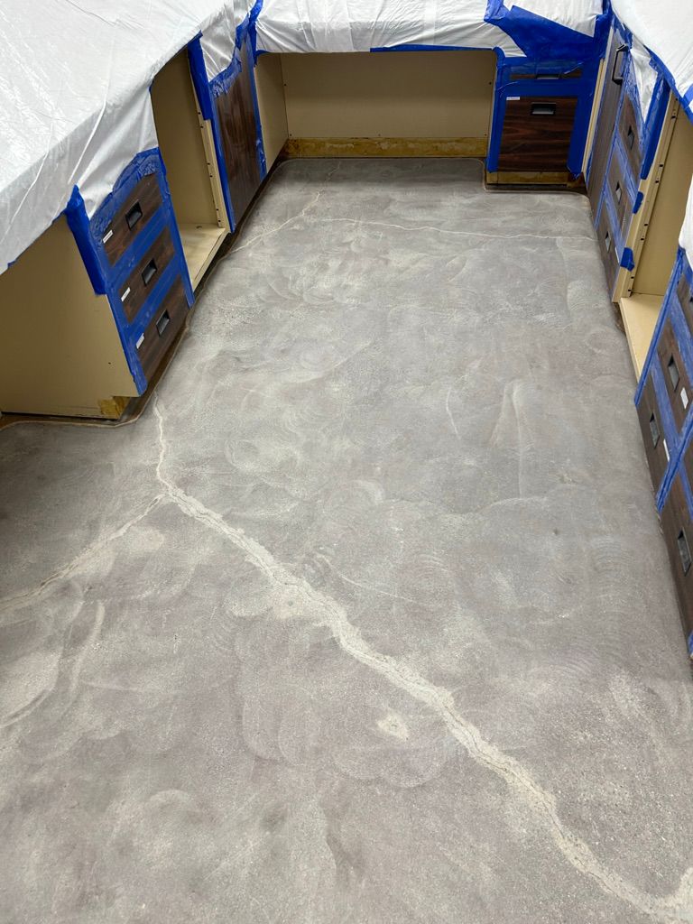 Close-up of a cracked pharmaceutical lab floor with cabinetry masked with painter's tape, prior to epoxy crack repair and resurfacing
