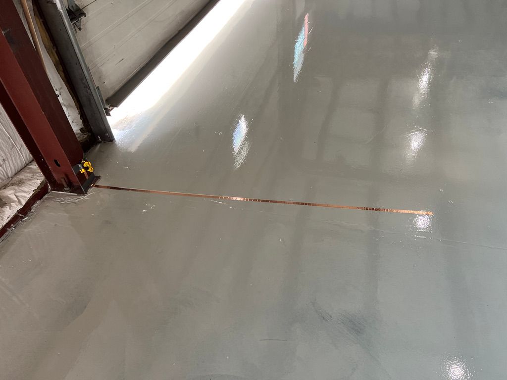 Smooth shiny gray ESD floor with copper grounding strip and red metal vertical beam beside white garage door panel