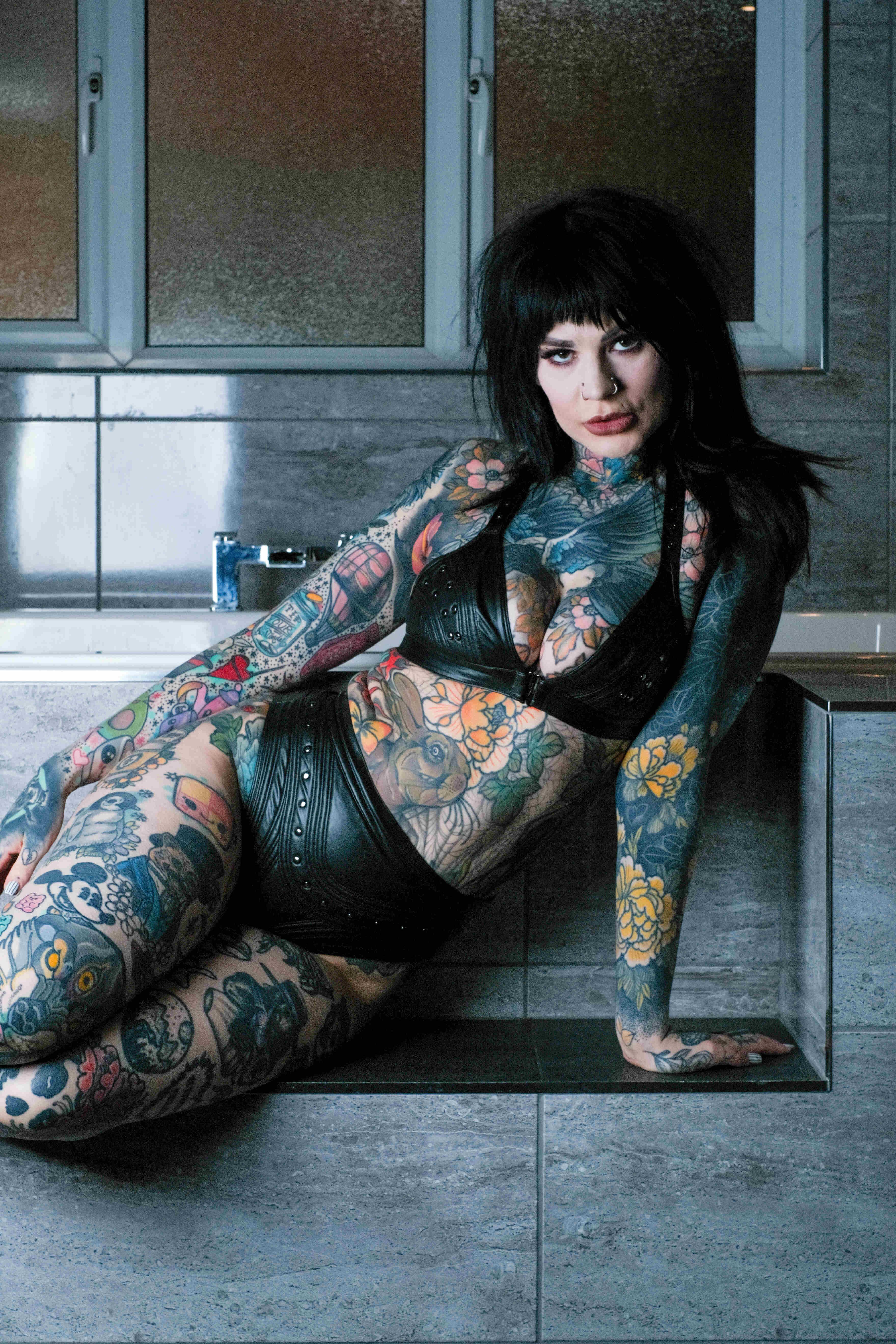 Tattooed model in leather outfit, bathroom setting