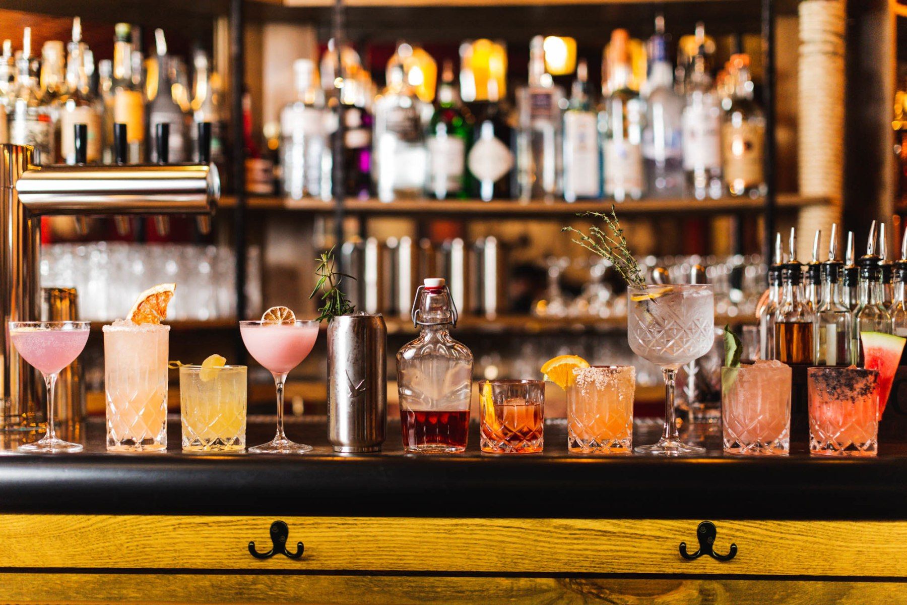 Furtivo Speakeasy — row of colorful craft cocktails on a wooden bar counter with garnishes, citrus, and herbs
