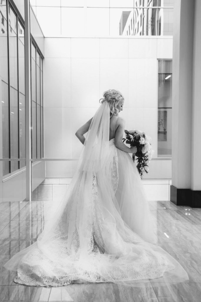 Bride in elegant gown with long train and cascading bouquet β black and white