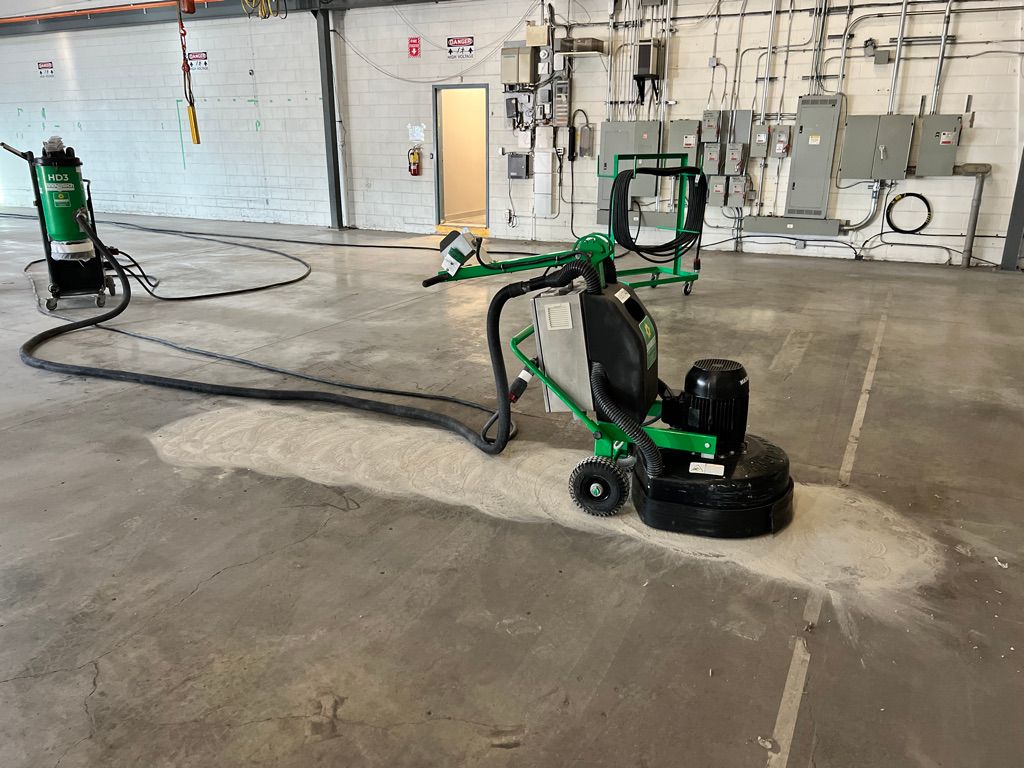 Industrial high-tech space with concrete floor being prepared — green floor grinder connected to HD3 vacuum with electrical panels on white brick wall