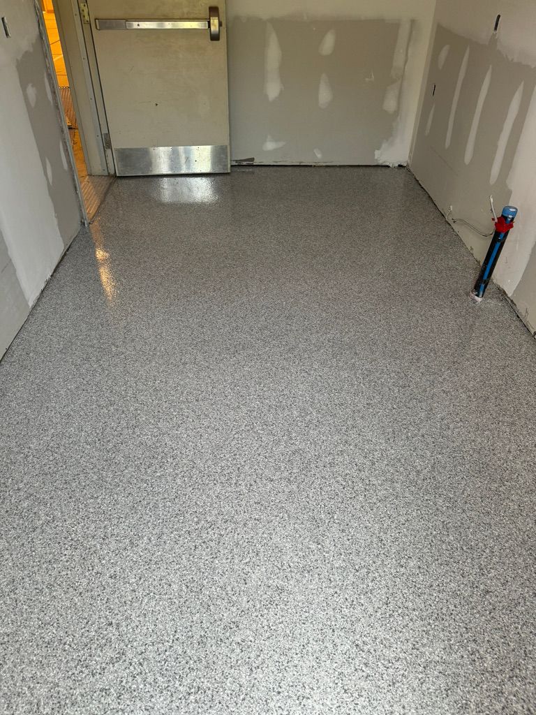 Small school room with freshly applied speckled gray epoxy floor, unfinished drywall and metal push-bar exit door