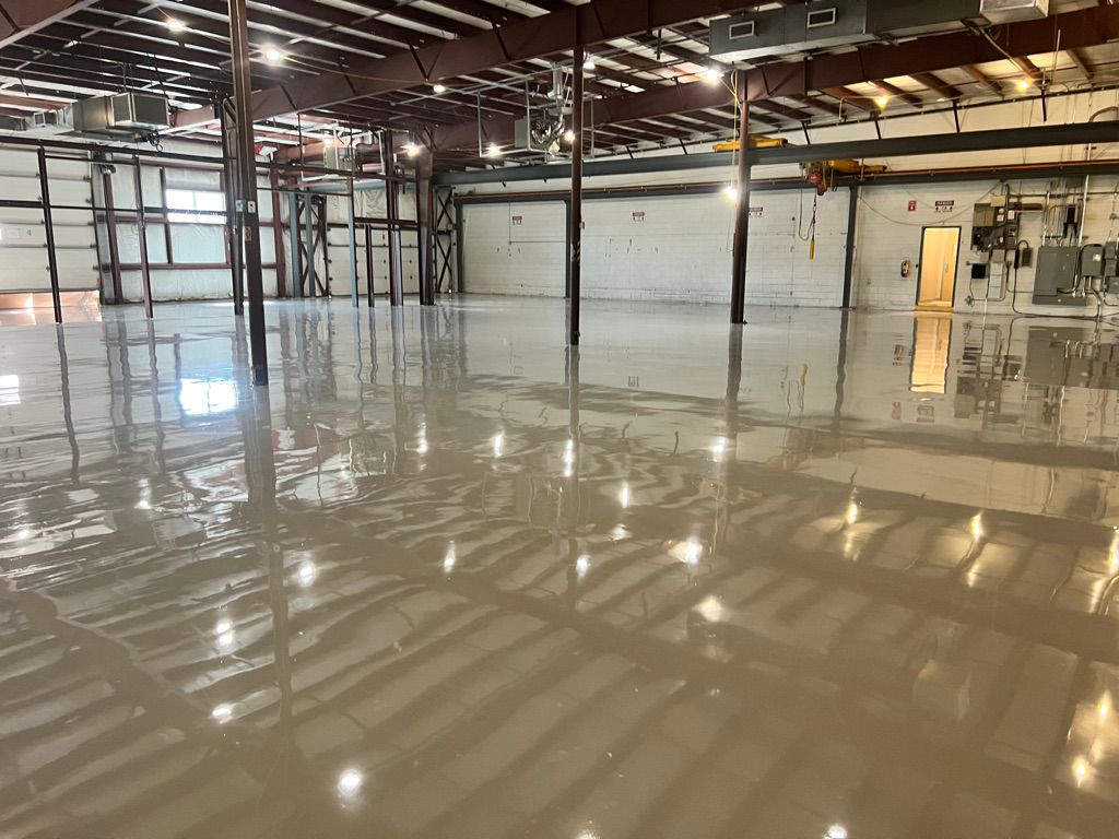 Large empty industrial warehouse with highly reflective smooth floor, metal support columns, garage doors and electrical panels